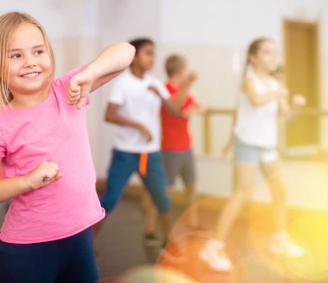 Positive girl exercising in group of classmates during dance class at school